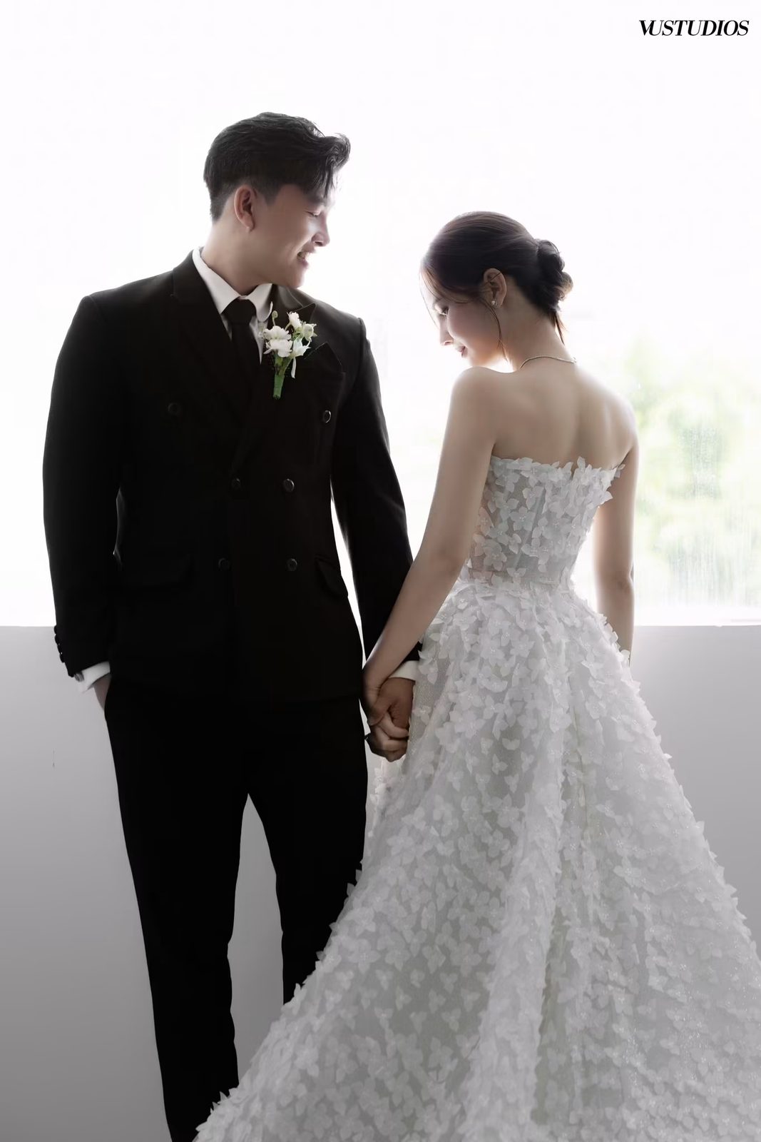 Chú rể suit hai hàng khuy cài hoa áo nắm tay cô dâu váy xòe phủ hoa nổi