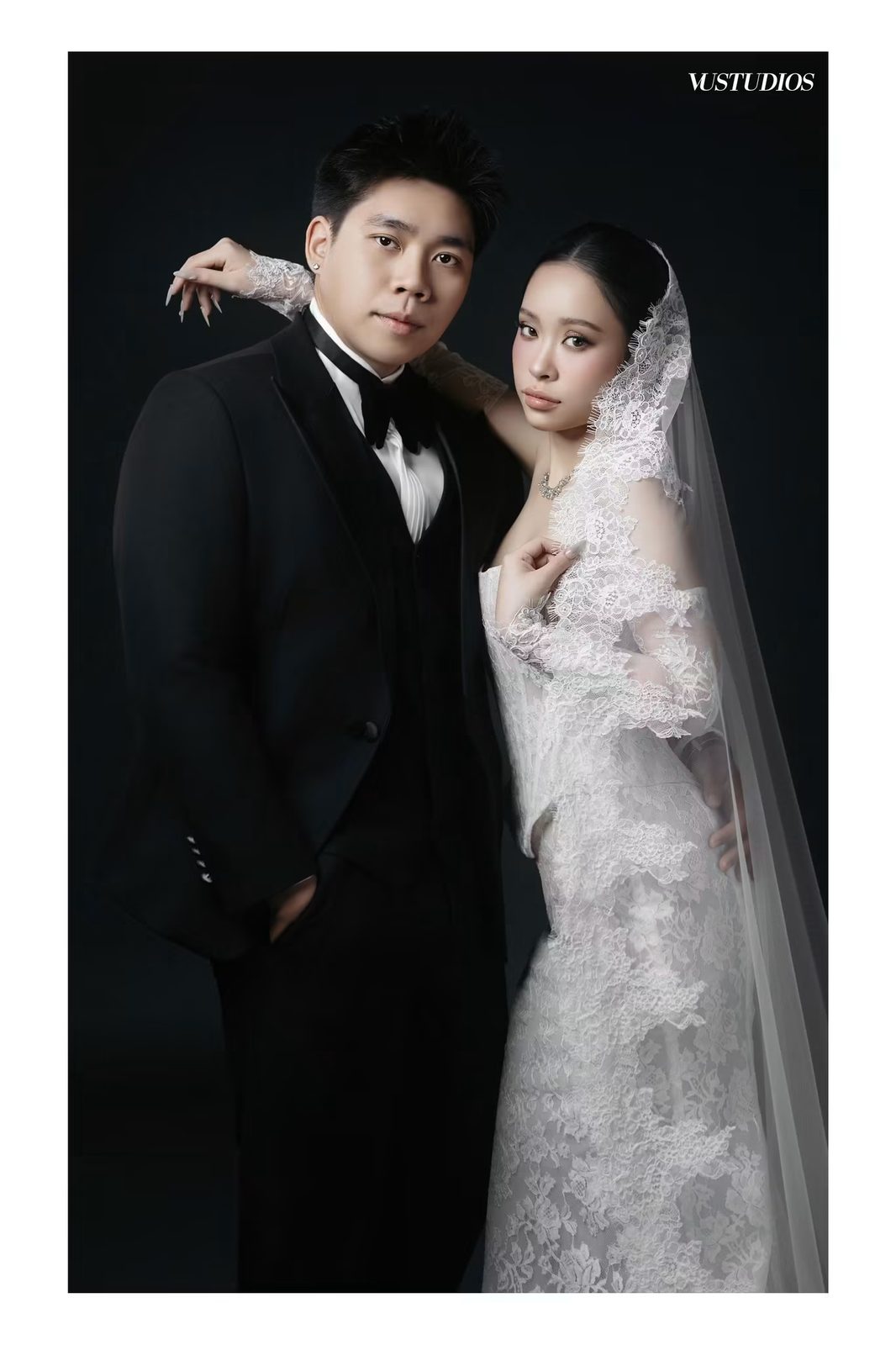 Chú rể suit đen ba mảnh nơ đen và cô dâu váy ren tay dài phủ voan trên nền tối