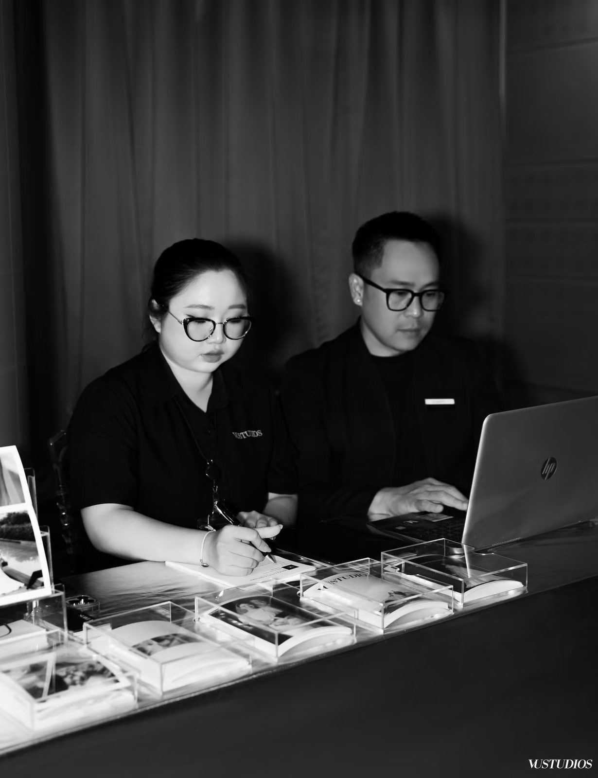 Ảnh đen trắng hai chuyên viên tư vấn ngồi làm việc với máy tính và mẫu vải tại VU STUDIOS