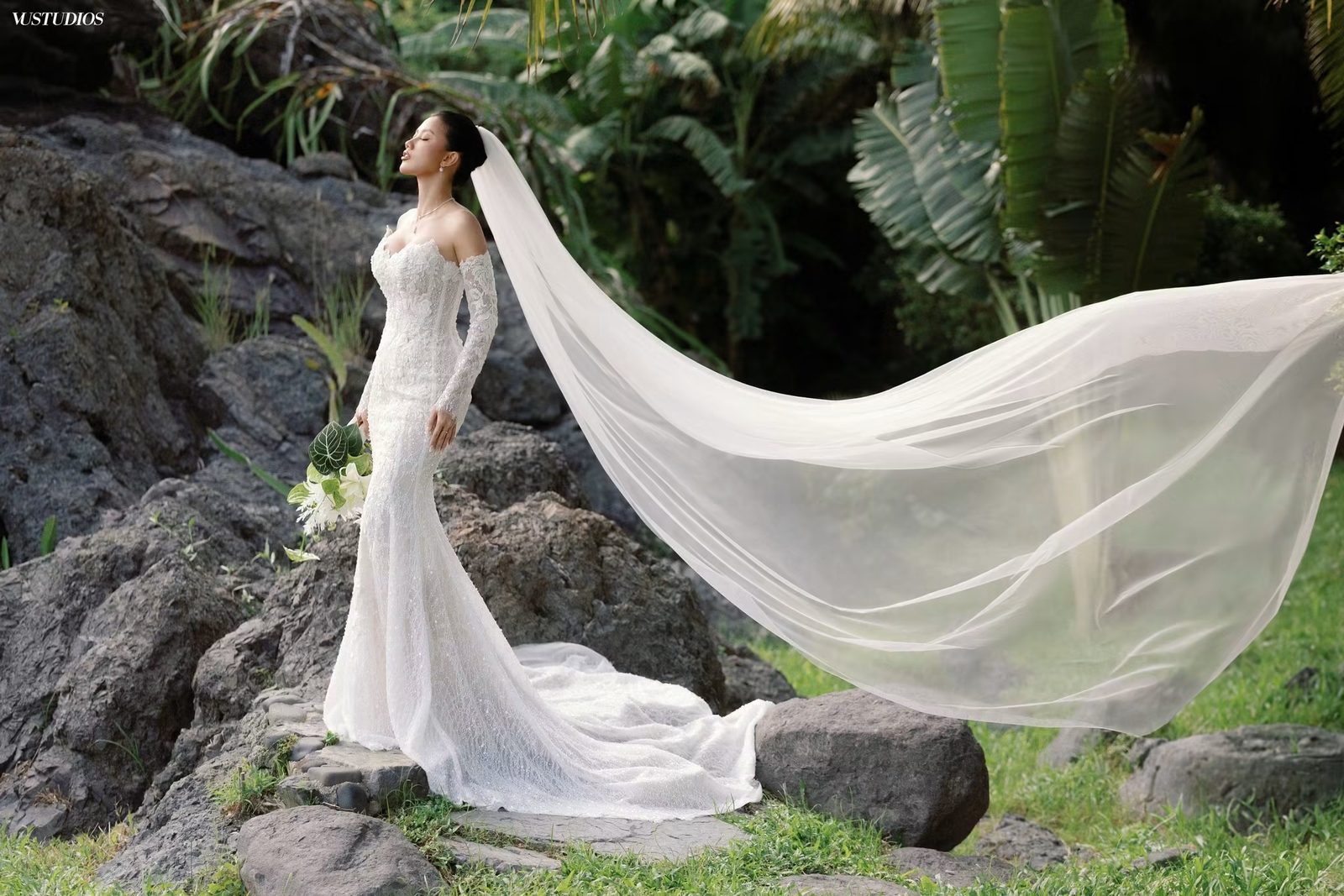 Cô dâu váy cưới ren Pháp tay dài đuôi cá với voan mỏng bay dài giữa khu vườn đá và cây xanh