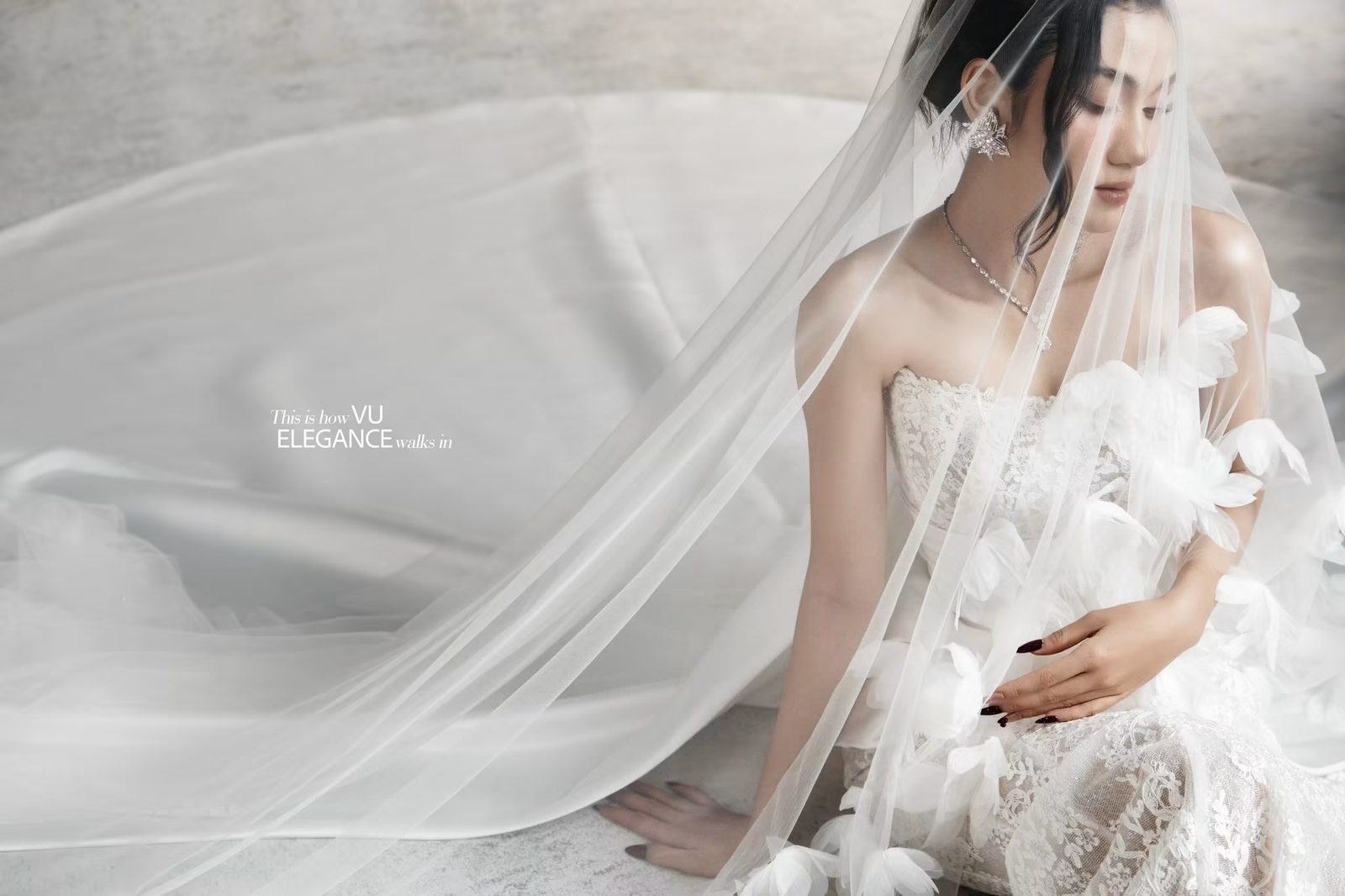 Cô dâu váy cưới ren cúp ngực phủ voan mỏng ngồi trên nền xám sáng
