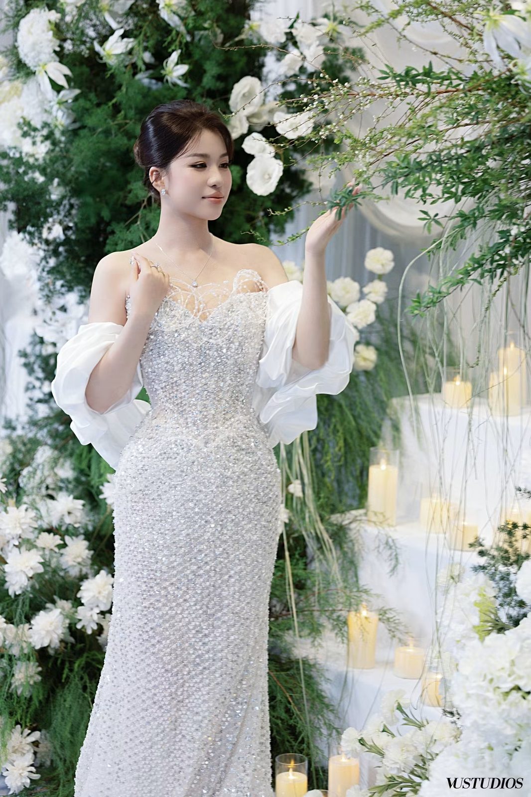 Cô dâu váy cưới trắng ngà đính kết lấp lánh bên hoa trắng và nến