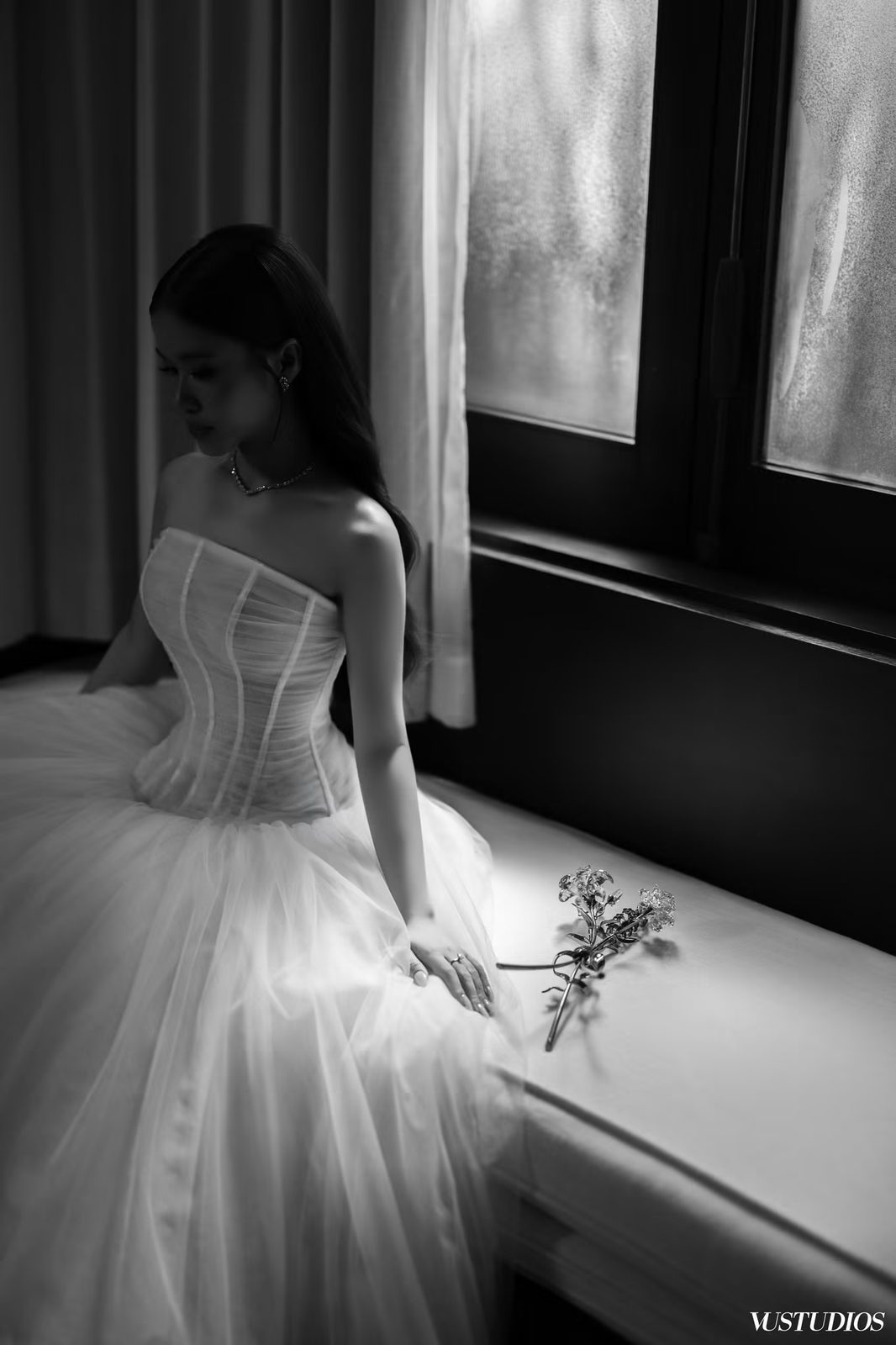 Ảnh đen trắng cô dâu váy cưới trơn corset chân váy tulle ngồi cạnh cửa sổ