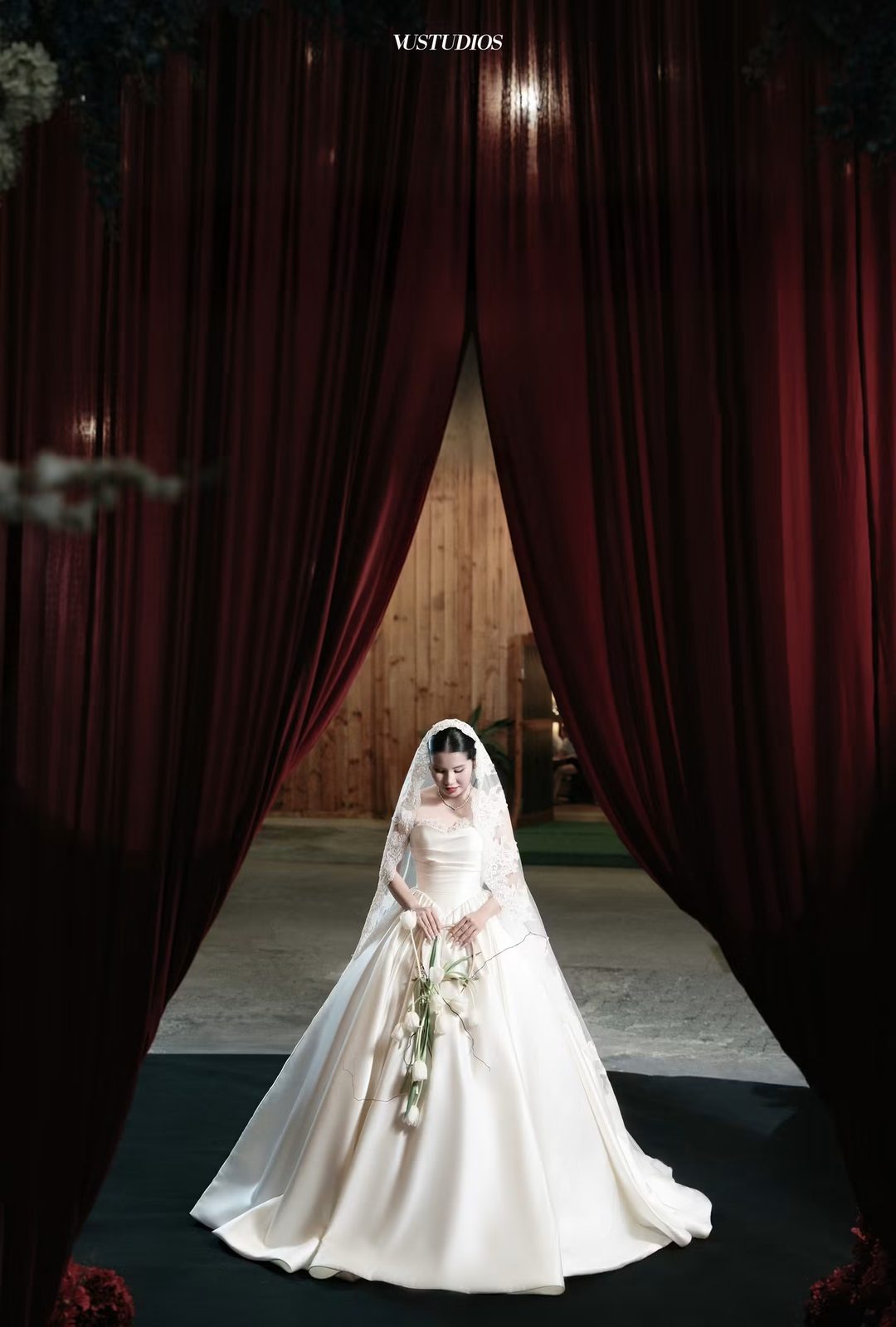 Cô dâu váy cưới trơn dáng xòe ballgown đứng trước phông rèm đỏ sẫm
